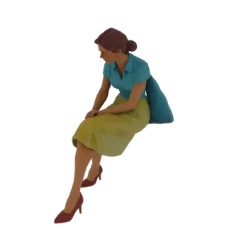 3D модель женщины в синей блузке с короткими рукавами и желтой юбке, сидящей с руками на коленях и смотрящей вниз.